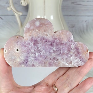 May include: A purple and white amethyst cloud shaped crystal. The crystal is smooth and polished with a natural, organic shape.