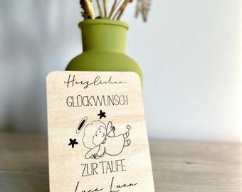 Może przedstawiać: Jasnobrązowa drewniana karta z napisem "Herzlichen Glückwunsch zur Taufe Luca Luan 09.02.2025" i rysunkiem anioła. Karta ma zaokrąglone rogi. W tle zielony wazon z kwiatami.
