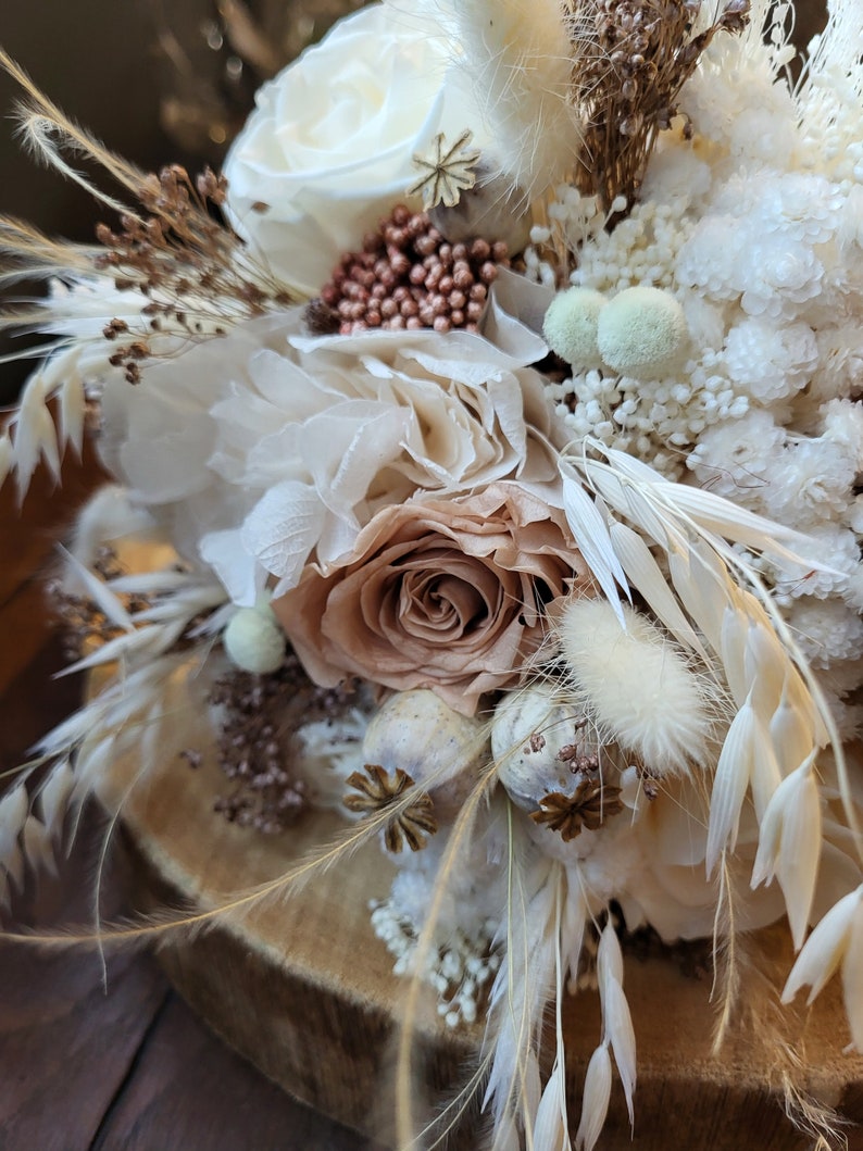 May include: A dried flower arrangement in a rustic style with white, beige, and brown tones. The arrangement features dried roses, pampas grass, and other dried flowers.