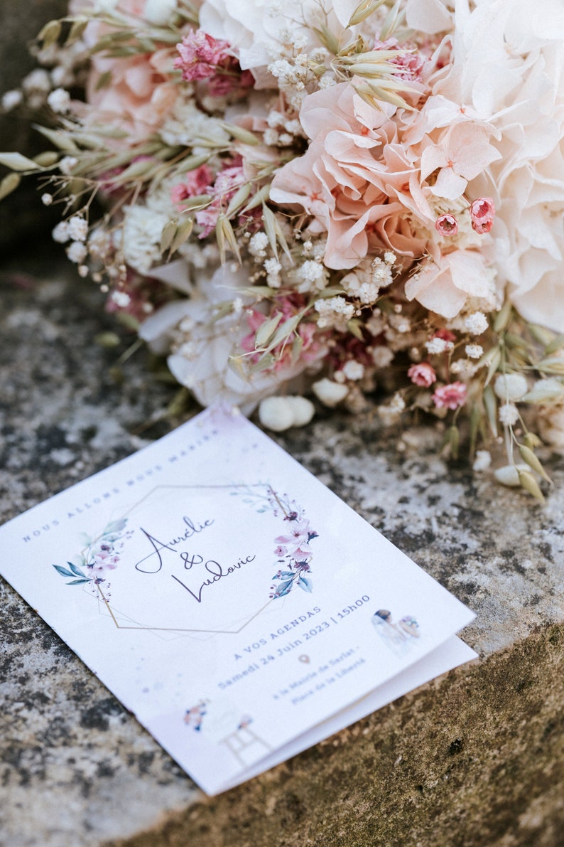 May include: A white wedding invitation with a gold geometric frame and floral accents. The invitation reads "Aurelie & Ludovic" and includes the date "Samedi 24 Juin 2023 | 15h00".