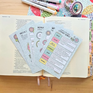 May include: A set of printed study cards featuring colorful charts on literary genres, prose, poetry, similes, metaphors, hyperbole, idioms, personification, and parables, fanned out over an open Bible with colorful page tabs and markers.
