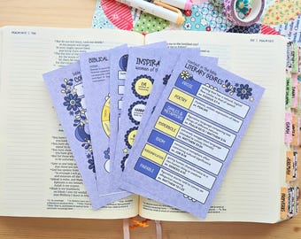 May include: A set of light purple study cards featuring printed text about biblical literary genres, including prose, poetry, and metaphors. The cards are fanned out on top of an open Bible with colorful index tabs and two rolls of washi tape.