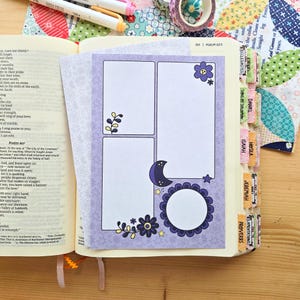 May include: A purple paper insert with three white rectangular and circular frames, decorated with dark purple flowers, a crescent moon, and small yellow stars, placed inside an open Bible with labeled book tabs.
