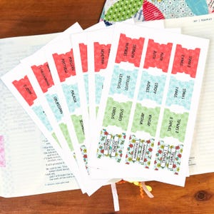 May include: A set of adhesive Bible index tabs printed on white paper with floral patterns in red, light blue, and light green. Each tab features a book name such as Genesis, Exodus, Leviticus, Numbers, Joshua, Judges, Ruth, 1 Samuel, 2 Samuel, 1 Kings, 2 Kings, Malachi, Colossians, 1 Thessalonians, 3 John, and Nehemiah.