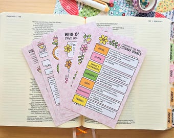 May include: A set of light pink study cards featuring floral illustrations and text about Bible literary genres, including prose, poetry, similes, metaphors, hyperbole, idiom, personification, and parables, resting on an open Bible.
