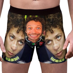 Op de afbeelding: Zwarte boxershort met een herhaald patroon van gezichten met een pleister op de neus. Het midden van de short heeft een close-up van het lachende gezicht. De short heeft een zwarte tailleband.