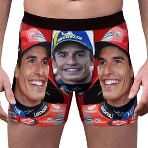 May include: Red boxer shorts with a smiling face printed on the front and sides. The shorts have a black waistband and a red background. The faces are wearing a red cap and a blue cap.