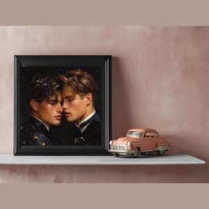 May include: A framed square print featuring two individuals with dark hair facing each other in a dark setting with gold flecks, positioned next to a small, vintage-style pink toy car. The artwork is encased in a simple black frame.