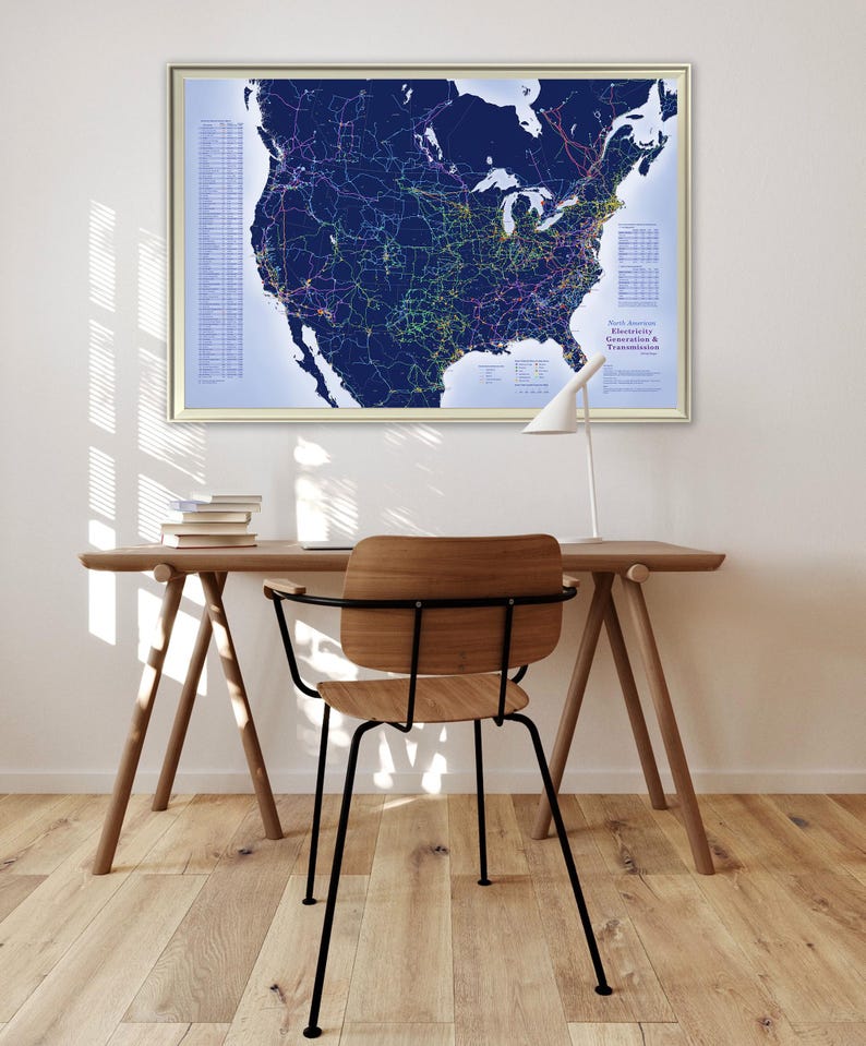May include: A framed map of North America, showcasing electricity generation and transmission lines. The map is predominantly blue with colorful lines representing the electrical grid. The frame is silver, and the map hangs above a wooden desk with a chair.