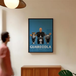 Könnte beinhalten: Gerahmtes Poster mit blauem Hintergrund, das eine Grafik eines Mannes zeigt, der drei Trophäen hält. Das Poster hat den Namen "GUARDIOLA" in weißer Schrift und einen schwarzen Rahmen. Der Text "2022-23" steht unter dem Namen.