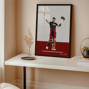 May include: Framed art print featuring a stylized illustration of a cricket player in a black and red uniform, holding a bat and helmet. The artwork has a red and gray background with a quote at the bottom.