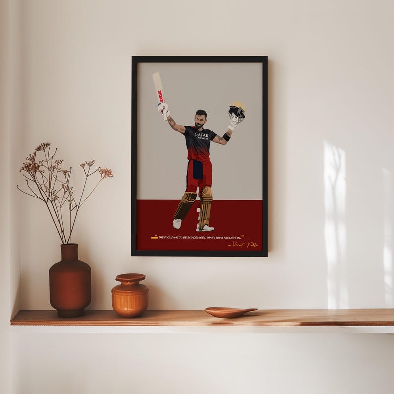 May include: Framed art print featuring a cricket player in a black and red uniform, holding a bat and helmet aloft. The artwork has a red and gray background with a quote at the bottom. The print is displayed on a wall.