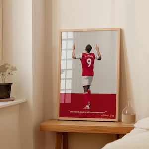 May include: A framed illustration of a soccer player in a red and white jersey with the number 9 on the back. The player is raising both arms in the air. The quote "When I have the ball at my feet, I'm in a different world." - Gabriel Jesus is printed below the illustration.