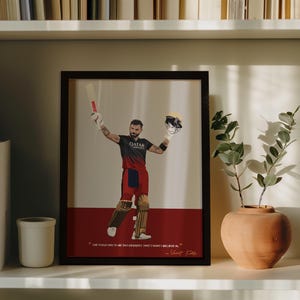 May include: Framed artwork featuring a cricket player in a black and red uniform, holding a bat and helmet. The artwork has a red base with text at the bottom and is displayed on a white shelf with a vase and plant.