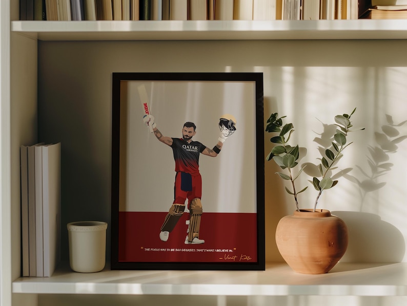 May include: Framed artwork featuring a cricket player in a black and red uniform, holding a bat and helmet. The artwork has a red base with text at the bottom and is displayed on a white shelf with a vase and plant.