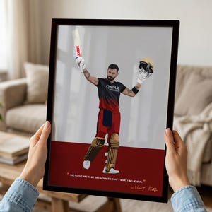 May include: Framed art print featuring a stylized illustration of a cricket player in a red and black uniform, holding a bat and helmet. The print has a white and red background with a quote by Virat Kohli. The frame is dark brown.