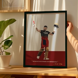 May include: Framed art print featuring a cricket player in a black and red uniform, holding a bat and helmet. The artwork has a white and red background with a quote by Virat Kohli. The frame is black.
