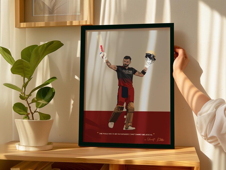 May include: Framed art print featuring a cricket player in a black and red uniform, holding a bat and helmet. The artwork has a white and red background with a quote by Virat Kohli. The frame is black.