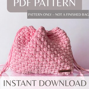 Può includere: Una borsa rosa con coulisse intrecciata, con il testo "PDF PATTERN" e "INSTANT DOWNLOAD". La borsa è realizzata in filato spesso e morbido e ha una piccola etichetta rettangolare. Il modello è per una borsa, non un prodotto finito.