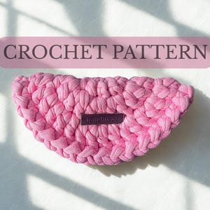 Può includere: Un modello all'uncinetto rosa, con la scritta "CROCHET PATTERN" in un rettangolo rosa. L'articolo fatto a mano ha la forma di una mezzaluna, con una piccola etichetta che dice "handmade".
