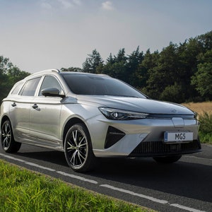 Könnte beinhalten: Ein silberner MG5 Elektro-Kombi fährt auf einer asphaltierten Straße mit grünem Gras und Bäumen im Hintergrund. Das Auto hat ein Nummernschild mit der Aufschrift "MG5".