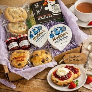 May include: A gift box containing scones, clotted cream, strawberry jam, and tea. The box has a tag that says "Handmade the Midlands". A cup of tea and strawberries are on the side, with a scone topped with cream and jam.