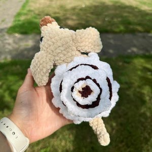 K&ouml;nnte beinhalten: Ein handgefertigtes H&auml;kel-Pl&uuml;schtier in Hundeform aus hellbraunem Garn, mit einem gro&szlig;en, spiralf&ouml;rmigen, wei&szlig;-dunkelbraunen blumenartigen Muster auf dem R&uuml;cken, einer kleinen braunen Nase und dunklen Augen aus weichem, strukturiertem Pl&uuml;schgarn.