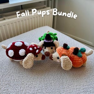 May include: Three crocheted puppy figures labeled Fall Pups Bundle. One puppy wears a red and white mushroom cap, another wears a black witch hat with green accents, and the third wears an orange pumpkin costume with green leaves.
