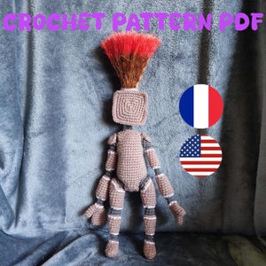 May include: A handmade crochet doll with a square head and a brown body. The doll has red and brown hair and is wearing grey and white striped accents on its limbs. The image includes the text "CROCHET PATTERN PDF".