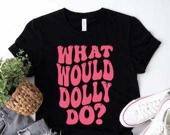May include: A black short-sleeved t-shirt featuring the pink text "WHAT WOULD DOLLY DO?" in a bold, rounded font. The shirt has a crew neckline and a standard fit, with the graphic centered prominently on the front of the garment.