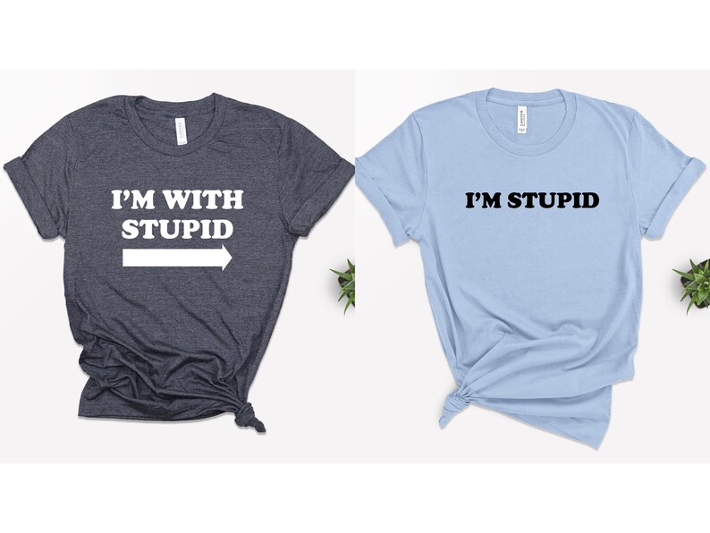 May include: Two t-shirts, one dark blue and one light blue, with a matching couple's design. The dark blue shirt says "I'M WITH STUPID" with a white arrow pointing to the right. The light blue shirt says "I'M STUPID" in black.