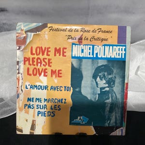 Op de afbeelding: Vintage vinylhoes voor Michel Polnareff's "Love Me Please Love Me". De hoes toont een portret van de artiest en tekst in het Frans, waaronder "Festival de la Rose de France" en "Prix de la Critique."