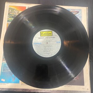 May include: Black vinyl record with a Cotillion Records label. The label features the text "Cotillion", "50 9040", "Emerson, Lake & Palmer", "Stereo", and "One".