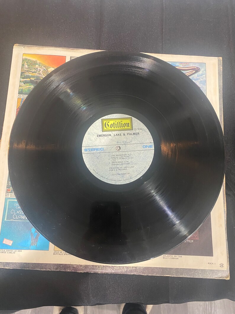 May include: Black vinyl record with a Cotillion Records label. The label features the text "Cotillion", "50 9040", "Emerson, Lake & Palmer", "Stereo", and "One".