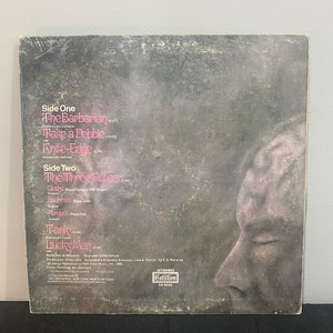 May include: Black and white album cover with a close-up of a person's face. The album is titled "Emerson, Lake & Palmer" and features the song titles "The Barbarian", "Take a Pebble", "Knife-Edge", "The Three Fates", "Clethe", "Lachesis", "Auropos", "Tank", and "Lucky Man".