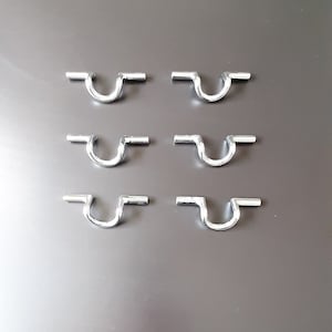 Könnte beinhalten: Sechs silberne Metallhaken mit U-förmigem Design. Die Haken sind in zwei Reihen zu je drei angeordnet.