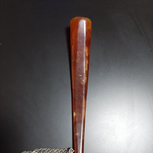 May include: A brown and silver shoe horn with a chain attached. The shoe horn is made of a smooth, polished material.