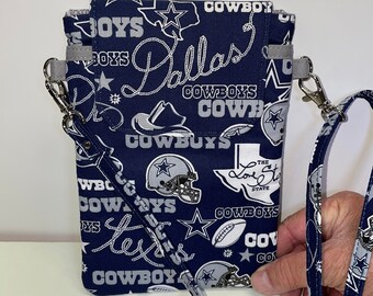 May include: A blue and silver crossbody phone purse with a Dallas Cowboys theme. The purse features a variety of Cowboys logos, including the star, the team name, and the state of Texas.