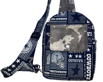 May include: A blue and white crossbody bag with a patchwork design featuring the Dallas Cowboys logo and the words "Dallas Cowboys". The bag has a large front pocket with a cowhide pattern.