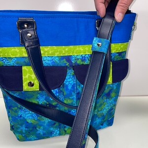 May include: A blue and green tote bag with a navy blue strap and a sea turtle print. The bag has a top zipper closure and two top handles.