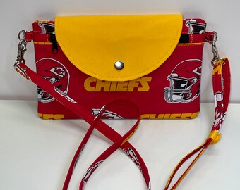 May include: Red and yellow fabric crossbody bag with a flap closure and a snap button. The bag has a white and yellow print of the Kansas City Chiefs logo and the word "CHIEFS".