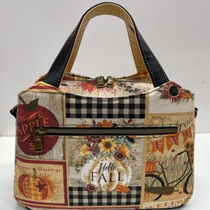 May include: A handbag featuring a patchwork design with autumn-themed prints including pumpkins, sunflowers, a bicycle, and apples. The bag has black handles, a top zipper closure, and a front horizontal zippered pocket with the text Hello Fall.