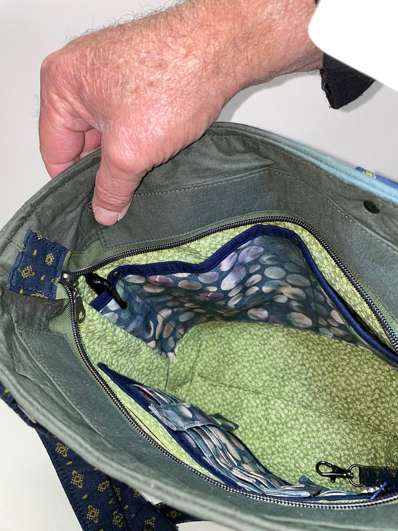 Może przedstawiać: Zielona torba typu tote z pł&oacute;tna z zamkiem błyskawicznym u g&oacute;ry i podszewką w niebiesko-białe wzory. Torba ma małą kieszeń wewnętrzną i klips na klucze.