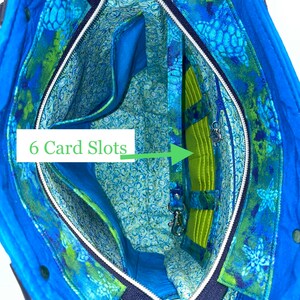 May include: Inside view of a blue tote bag with a zip closure. The bag has a green and blue floral print with a green lining. The lining has six card slots and a zipped pocket.