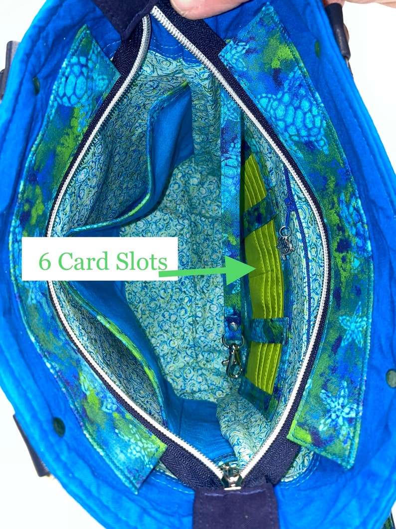 May include: Inside view of a blue tote bag with a zip closure. The bag has a green and blue floral print with a green lining. The lining has six card slots and a zipped pocket.