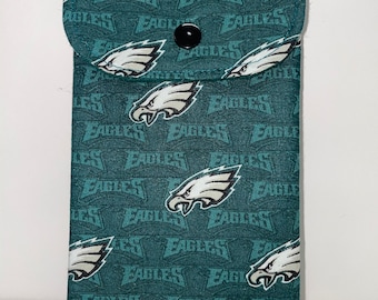 May include: A teal fabric glasses case featuring a repeating pattern of the Philadelphia Eagles logo and the word "EAGLES." The case has a flap closure secured by a black button. The case is rectangular and appears to be handmade.