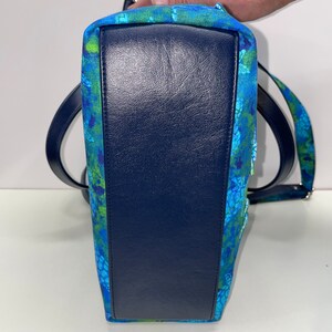 May include: A blue and green patterned tote bag with a dark blue leather base. The bag has a single strap and a zip closure.