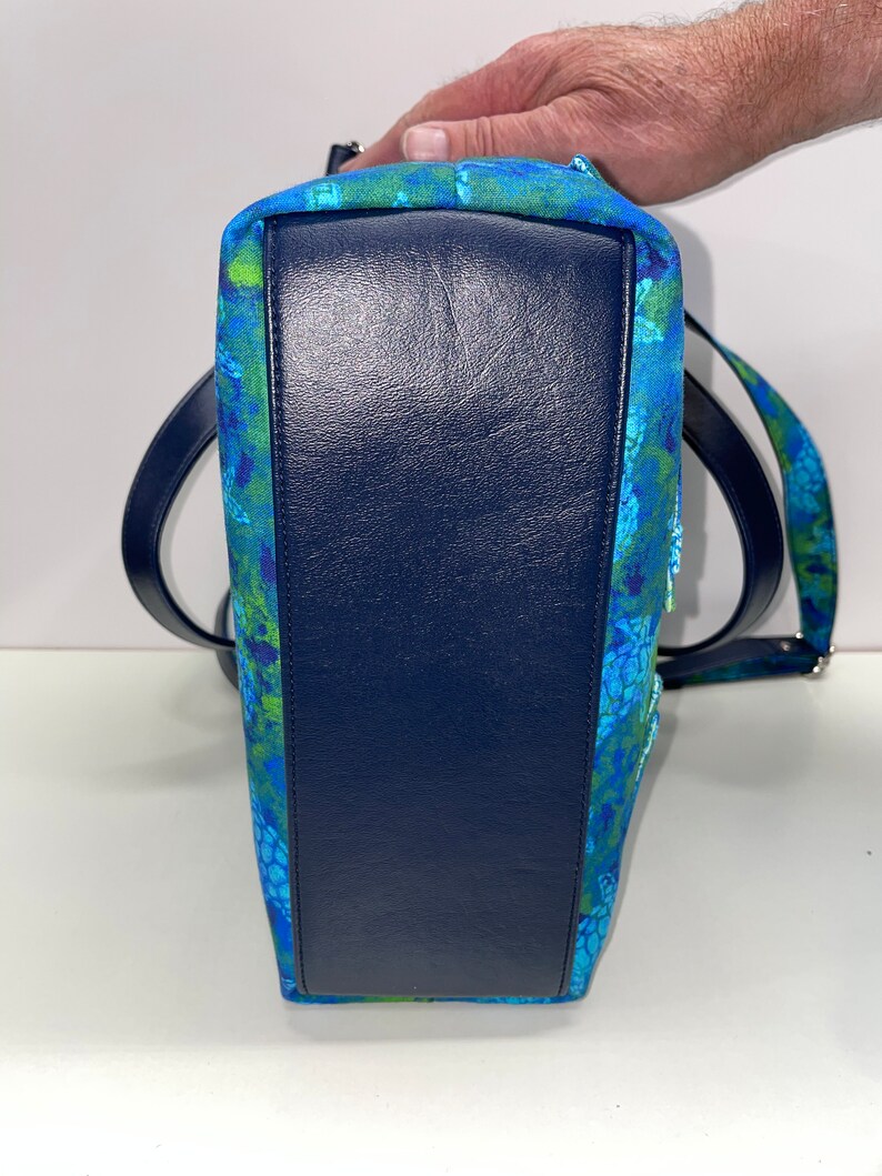 May include: A blue and green patterned tote bag with a dark blue leather base. The bag has a single strap and a zip closure.