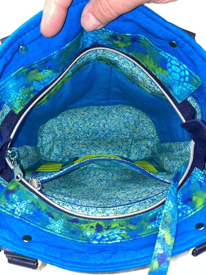 May include: The inside of a blue tote bag with a zipped pocket and a green and blue floral print lining.