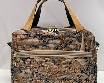 May include: A brown and green handbag with a winter scene print. The bag has two top handles and a detachable shoulder strap. The bag has a zipper closure and two additional zippered pockets on the front.